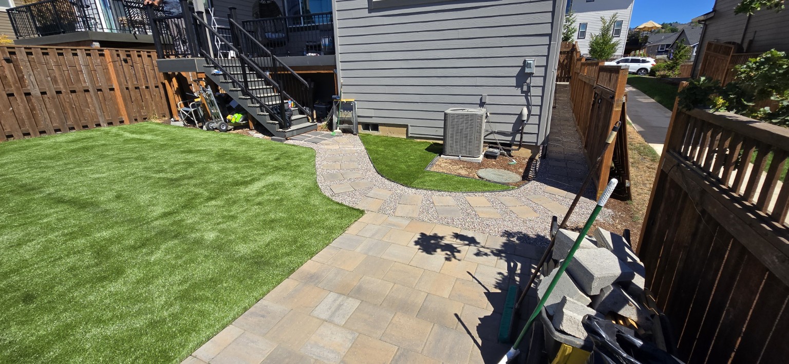Backyard with green turf, curved paver paths and a staircase with black railings